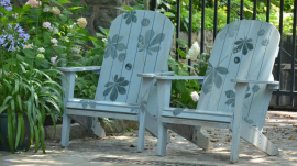 two adirondack chairs painted with flowers with a metal fence behind