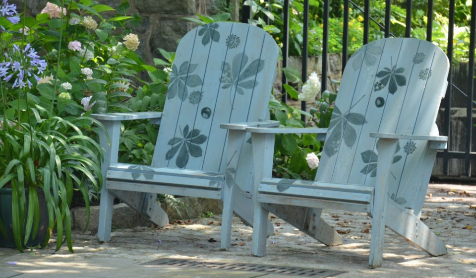 two adirondack chairs painted with flowers with a metal fence behind