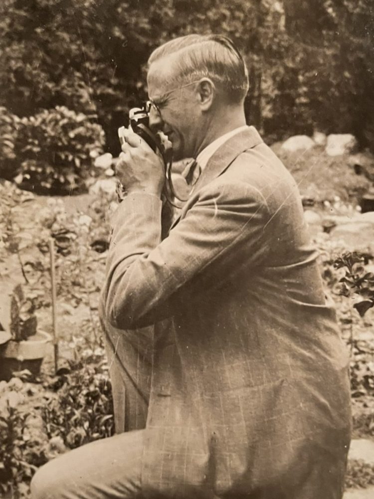 sepia photo of man in a suit taking a picture with a vintage camera from 1939